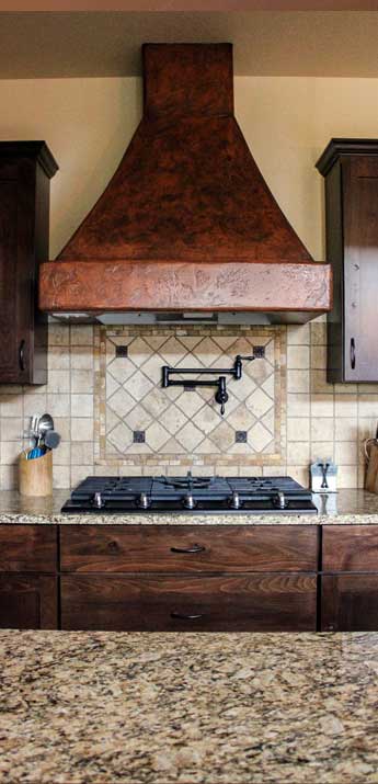 stove top with pot filler and rustic copper range hood and travertine backsplash